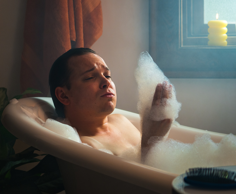 Male taking a bubble bath and looking at the foam