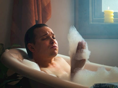 Male taking a bubble bath and looking at the foam