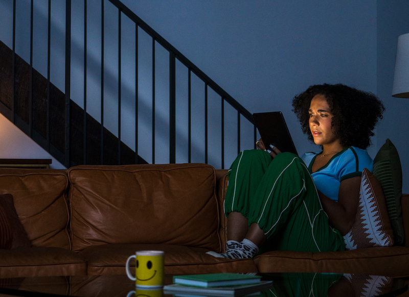 Female seating on the couch in the dark room, looking at her tablet