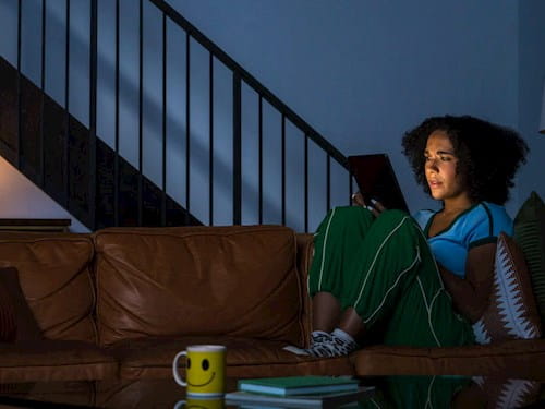 Female seating on the couch in the dark room, looking at her tablet