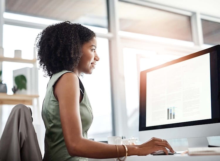 Young female is sitting at her desk and reviewing materials for CFP® Exam Certification on her computer