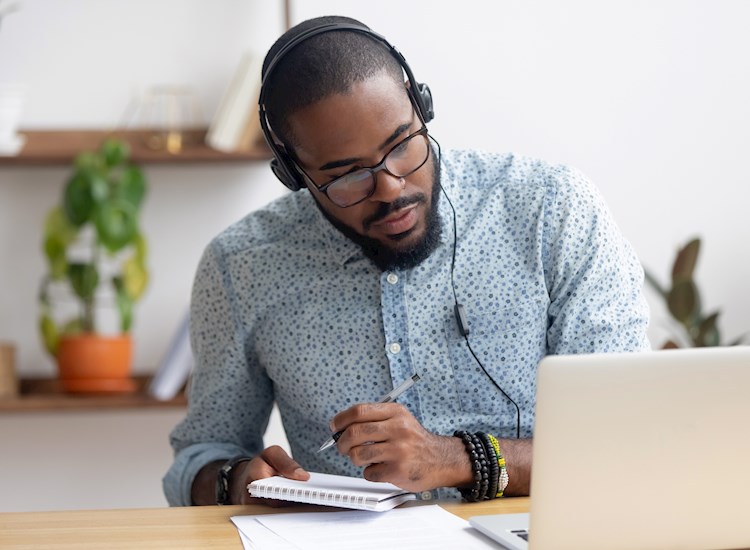 A dark-skinned male is taking notes while listening to materials for CFP® Exam Certification